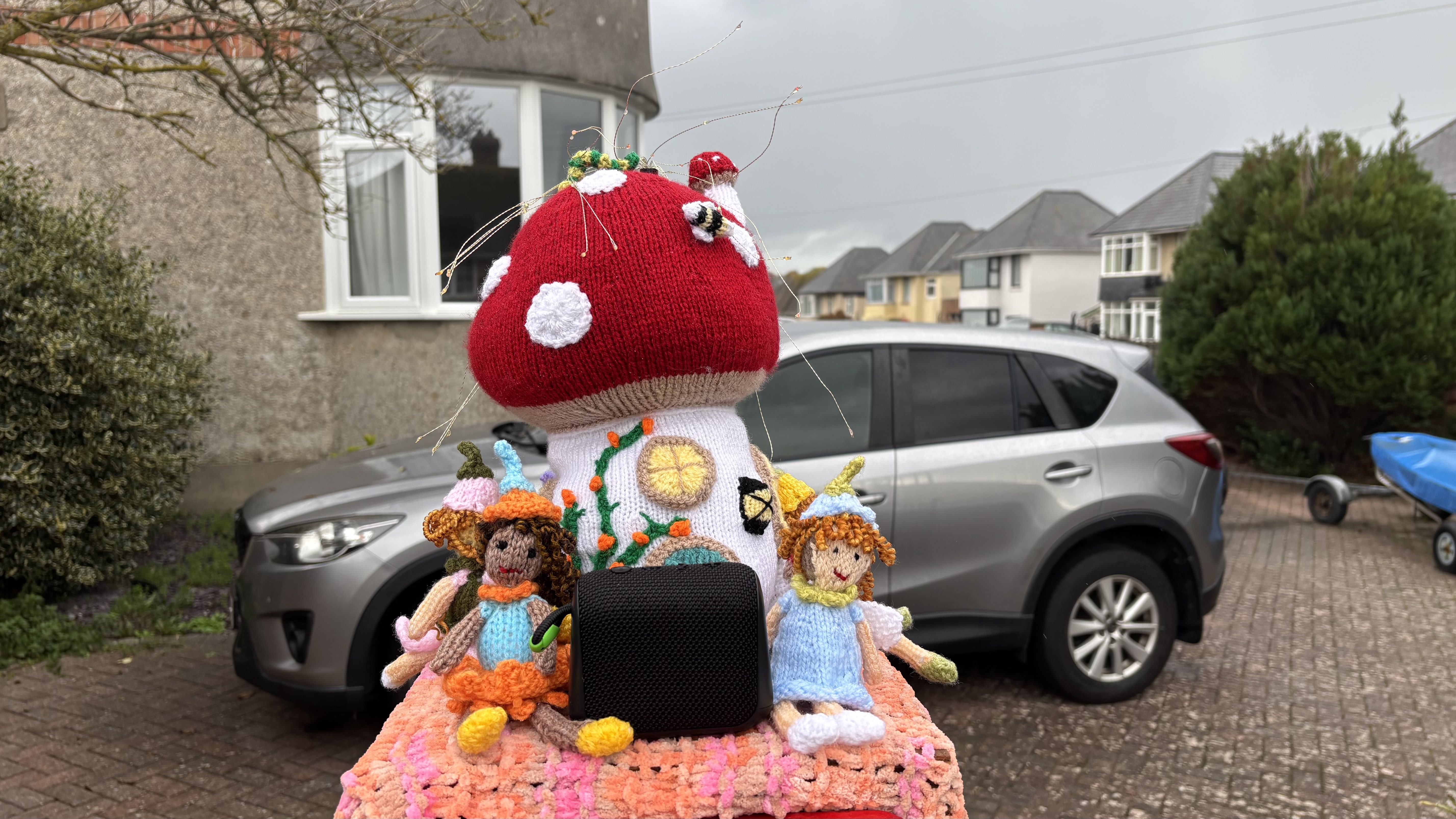 Black AO mini portable wireless speaker as part of a knitted autumnal post box cover