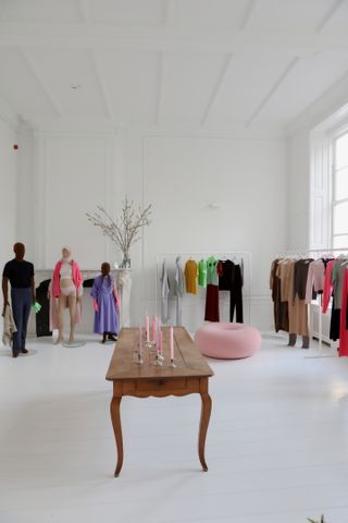 The Extreme Cashmere showroom. A room with mannequins and clothing rails behind a wooden table with different coloured candlesticks on it.