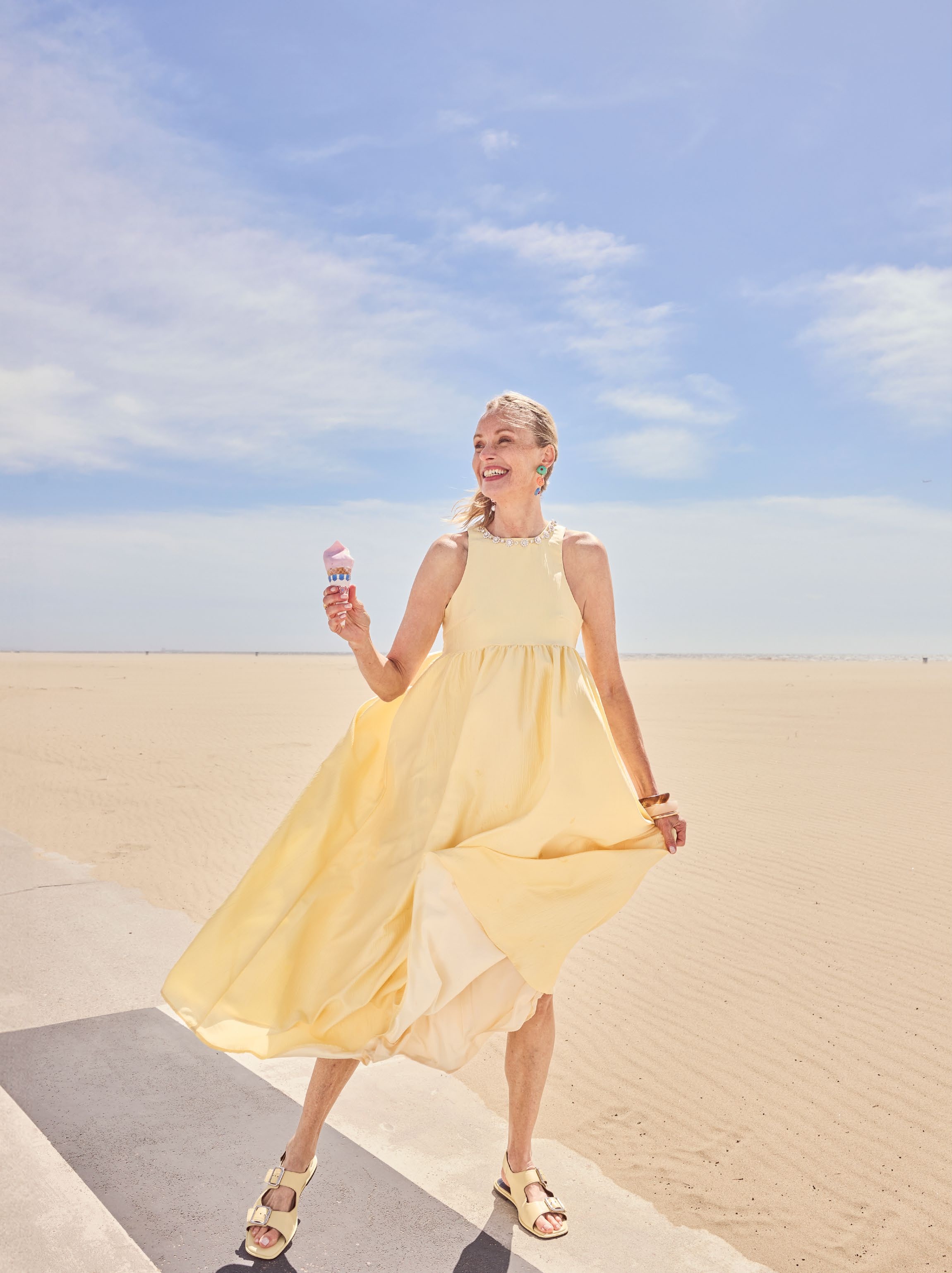 woman standing by the beach smiling broadly, wearing a pastel yellow dress