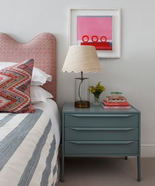 bedroom with red patterned headboard, ethnic patterned cushion, gray striped throw, pink artwork and aqua bedside chest