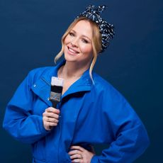 Kimberly Walsh wearing a blue jumpsuit with a paintbrush in her hand