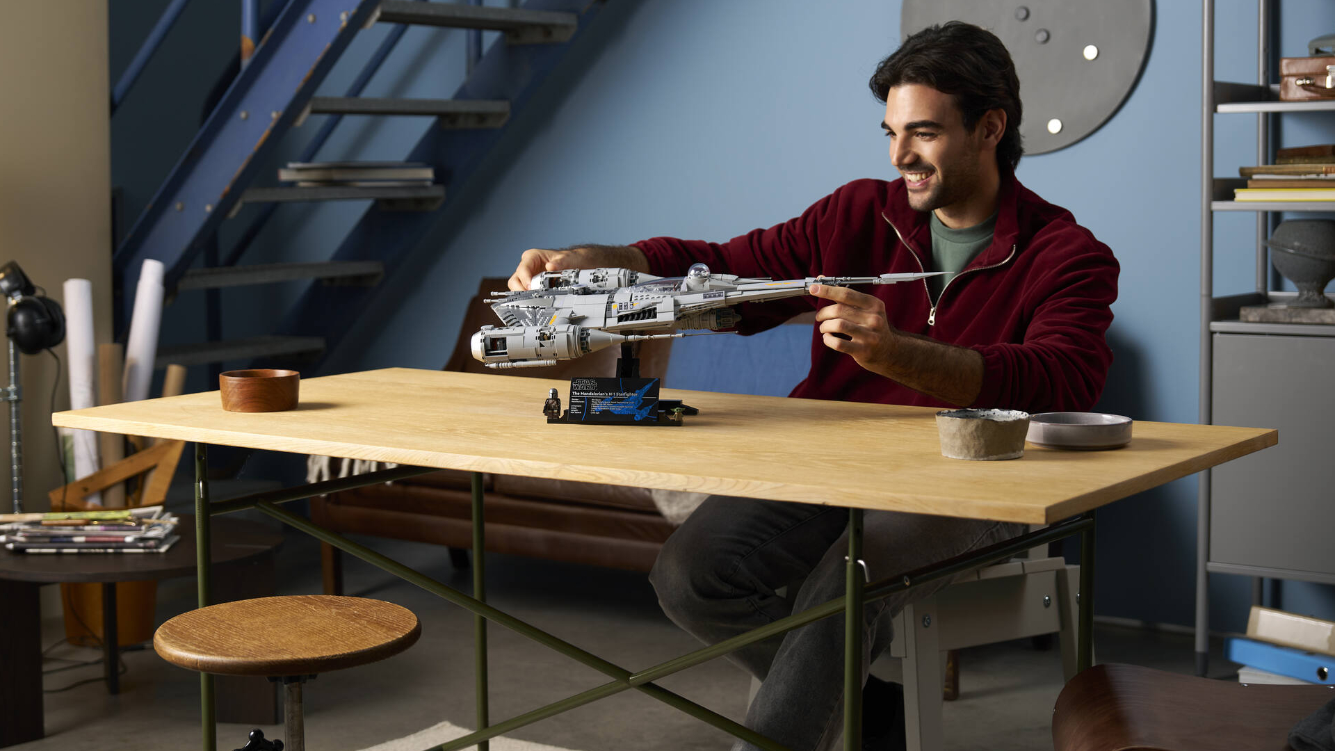 A man smiles while holding the Lego N1 Starfighter while seated at a wooden table