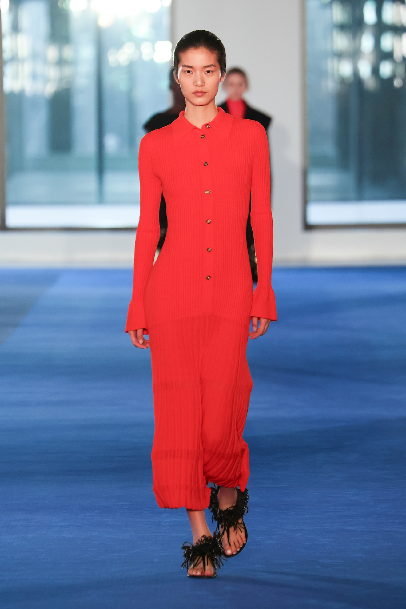 a model at Proenza Schouler Fall 2026 wearing a bright red-orange persimmon colored dress