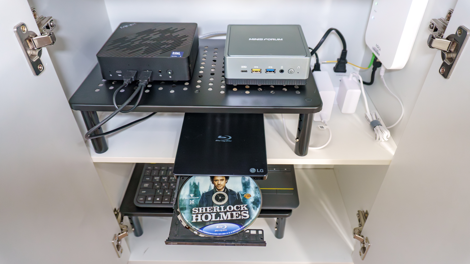 Two mini PCs and a portable Blu-Ray ripper inside a closed compartment on the bottom of a kitchen pantry cabinet