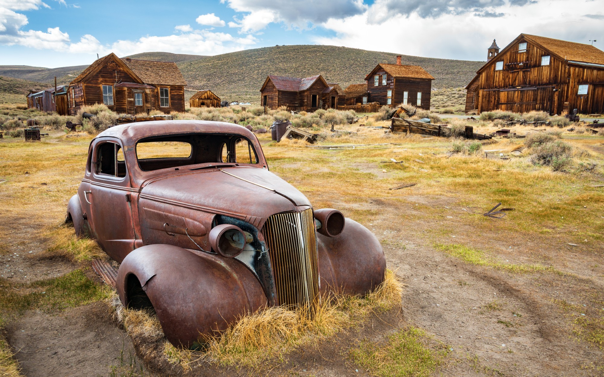 An old rusted car in front of old buildings in Bodie, California