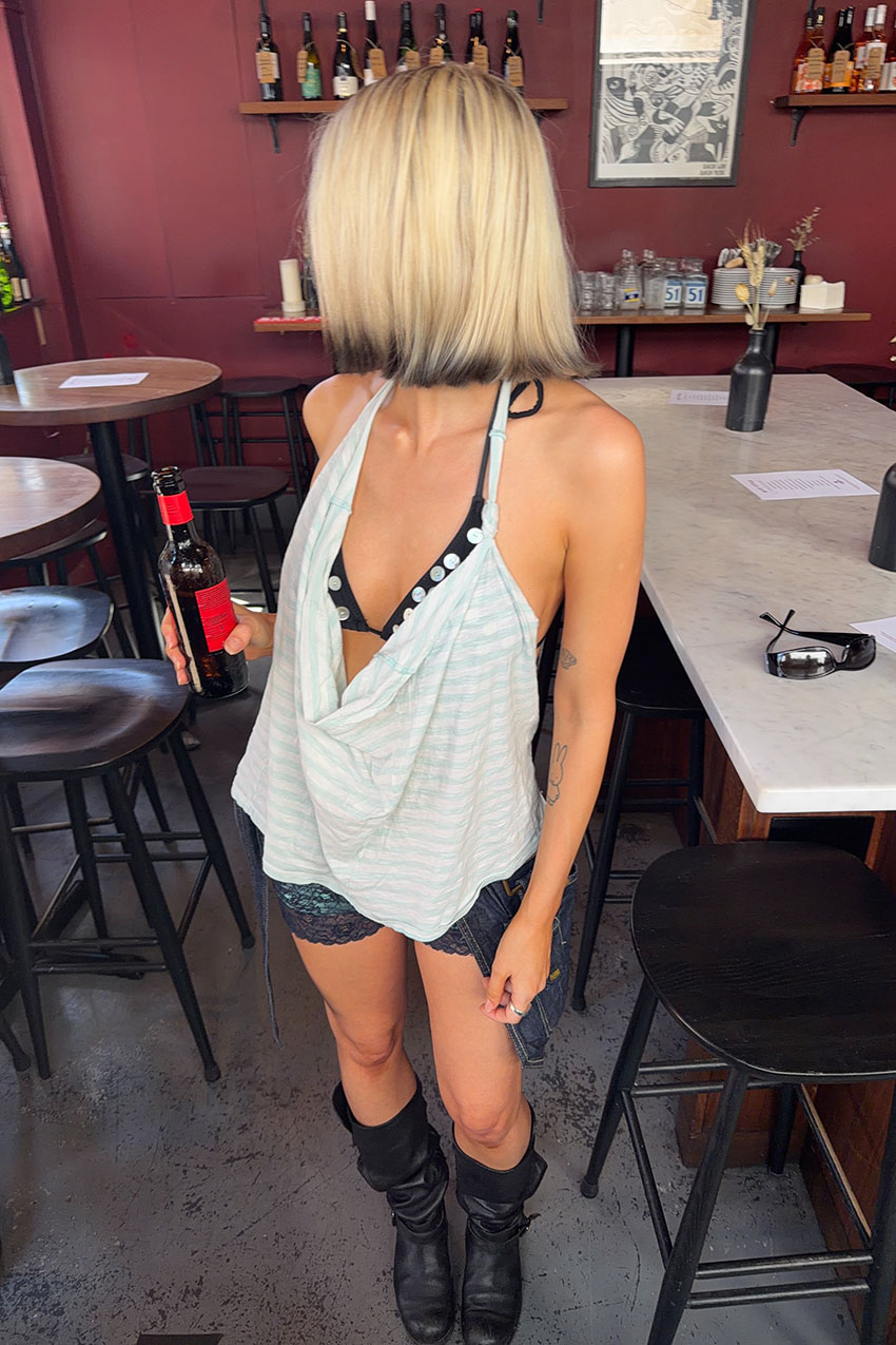 A woman wearing a striped tank top, button bathing suit top, black boots, lace shorts, and a denim utility belt.
