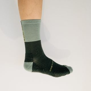 A white leg wears a two-tone green cycling sock against a white background