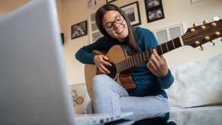 Woman plays acoustic guitar in front of her laptop