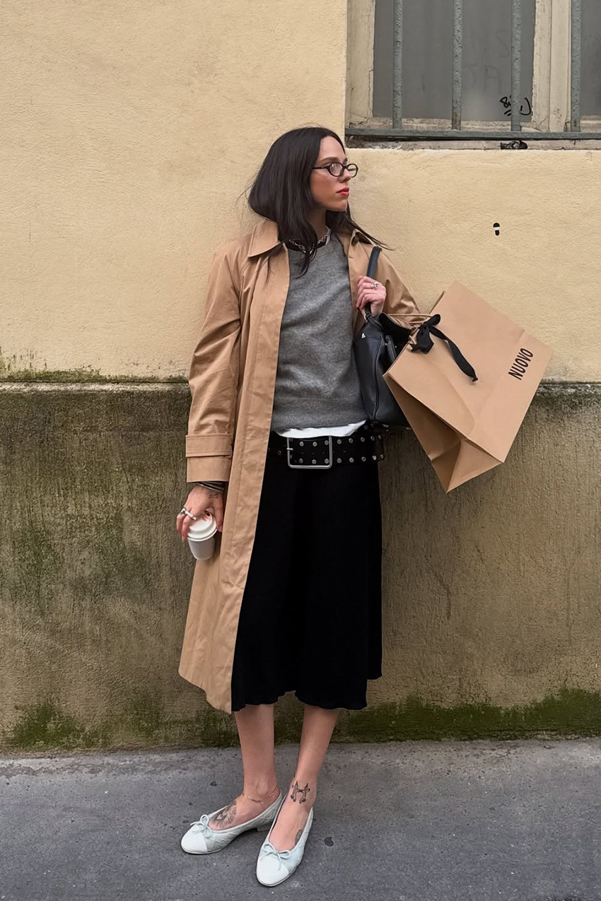 a woman wearing a trench coat, gray sweater, black culottes, and white flats
