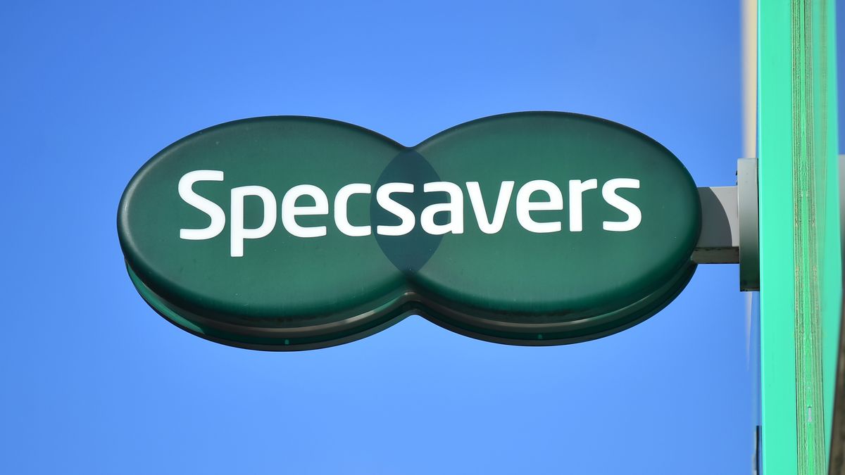 The Specsavers logo on a high-street sign, against a blue sky.