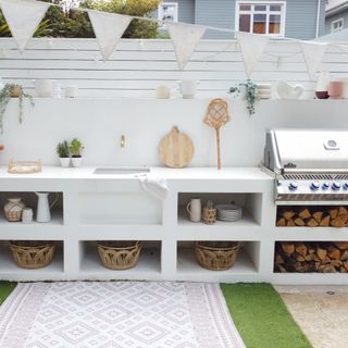 white outdoor kitchen with BBQ, sink, purpose built, seamless design, storage sections, rug, baskets, logs, white bunting