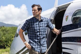 Death In Paradise season 13 episode 7: a close-up shot of Neville (Ralf Little) standing on the steps of a small charter plane, looking back out into the distance