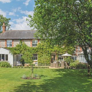 Luscious garden with lawn and trees looking towards a large cottage