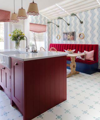 eclectic kitchen with deep red island, blue patterned floor tiles, green wall lights, blue and white wallpaper, banquette seating in red, pendant lights