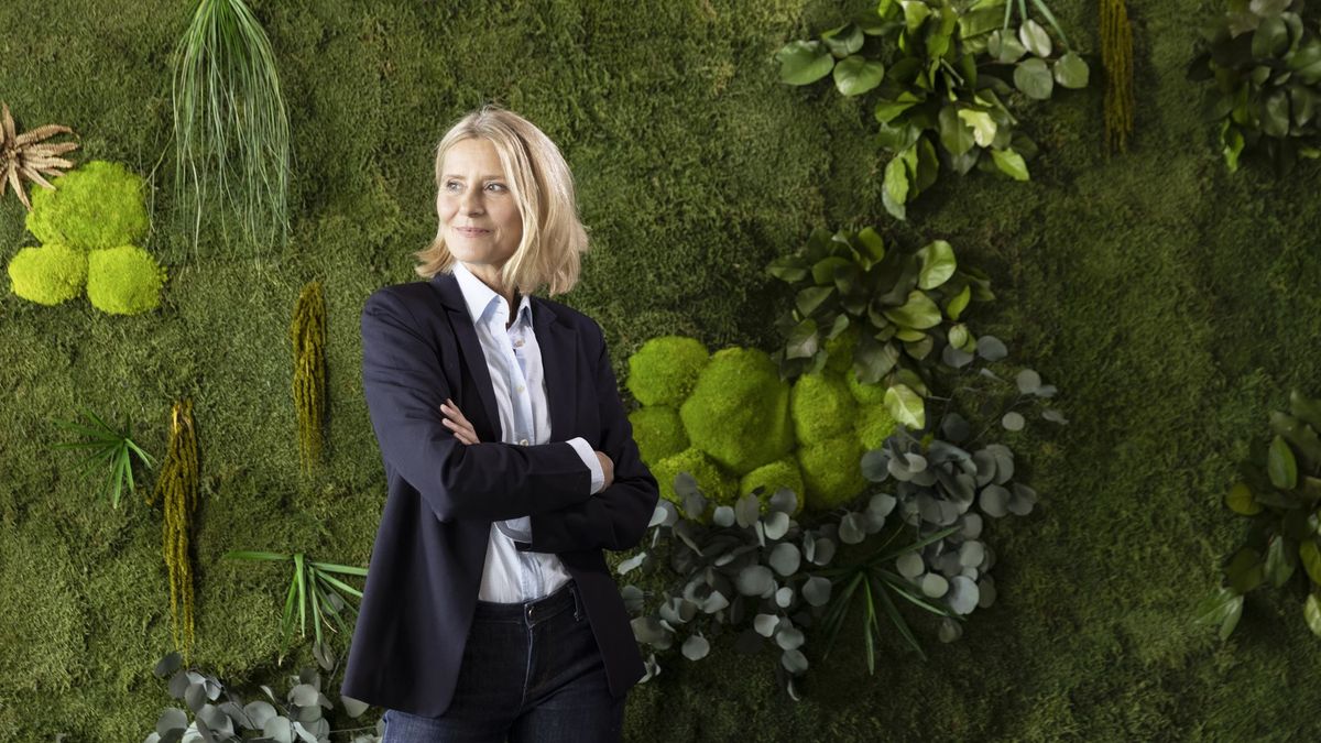 A business woman standing with her arms crossed in front of a wall of green plants