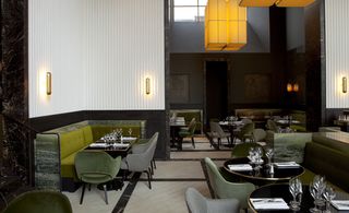 Monsieur Bleu, Paris, France. A restaurant with green "L" shaped seating booths with tables and chairs around them, wall lights and large square yellow pendant lights above.