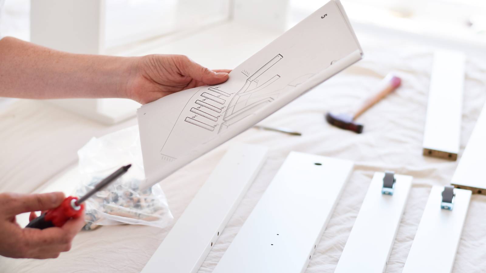 hands holding instructions and screwdriver above pieces of flat pack furniture