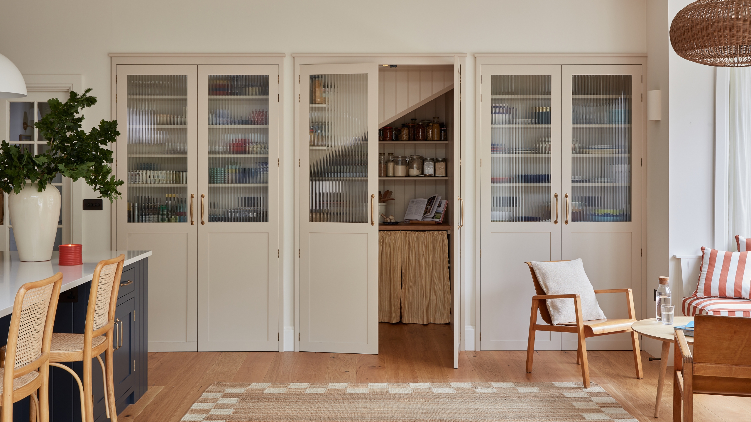 A large pantry installed beneath the stairs, with white and ribbed glass doors