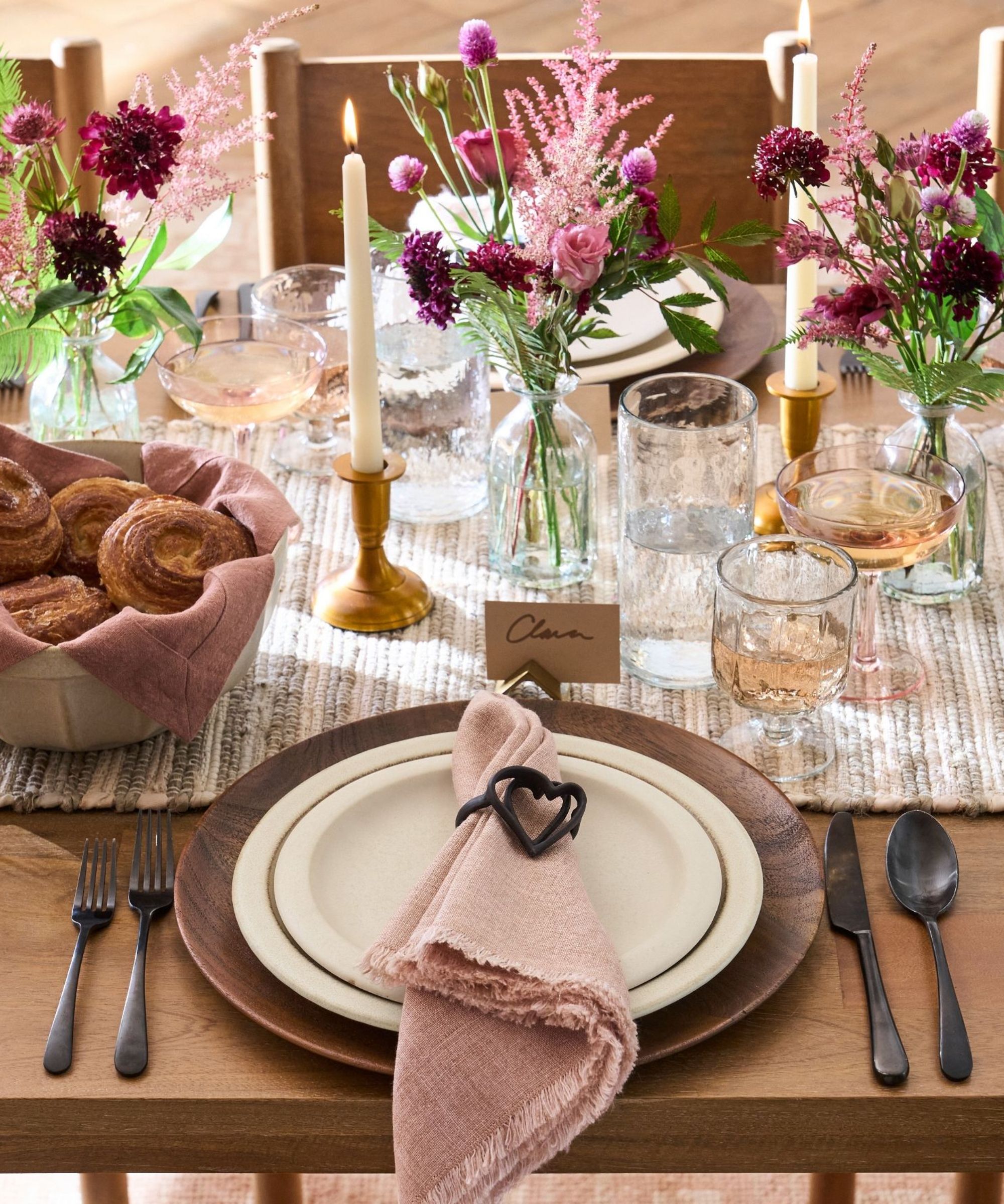 Wooden dining table with grey striped runner, wooden charger plates, white stoneware, pink napkins and black cutlery