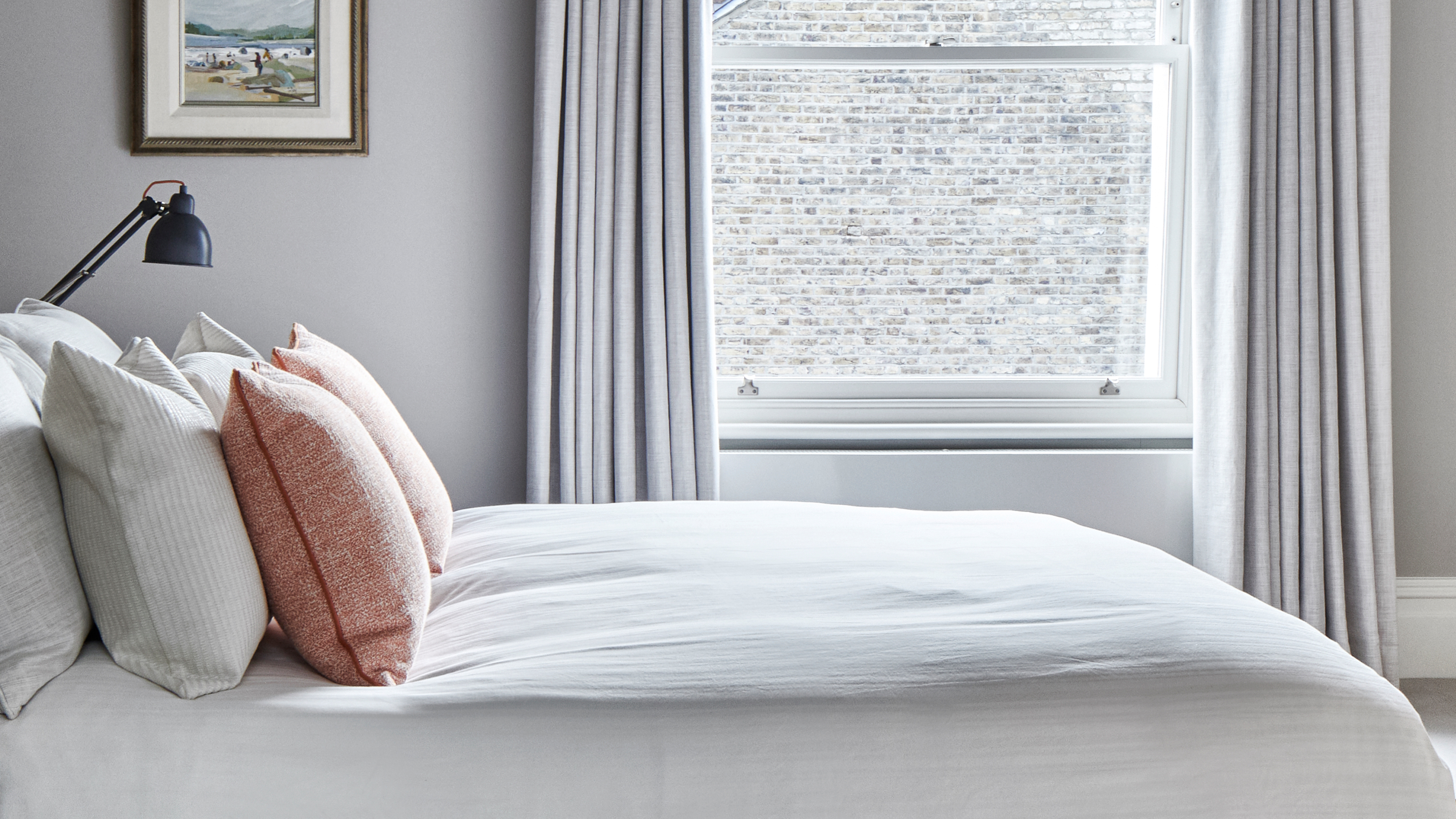 A bedroom with a bed in front of a large sash window. The bed has white and orange pillows and a white duvet cover