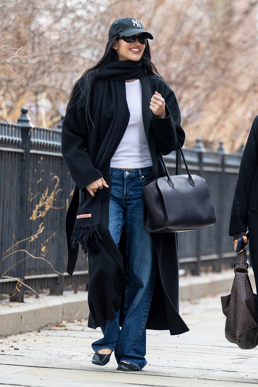 Amelia Gray wearing a Yankees baseball cap, black scarf and coat, white T-shirt, baggy jeans, and black glove flats