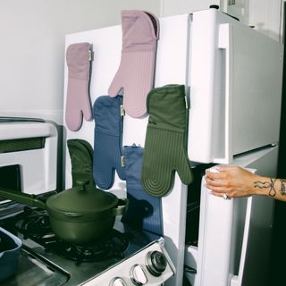Oven gloves in assorted colours hung up on side of fridge above stove in kitchen