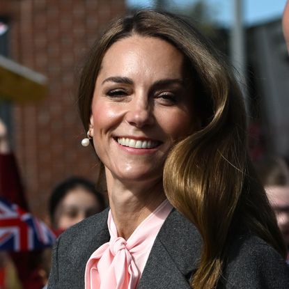 Kate Middleton wearing a gray suit and pink blouse smiling