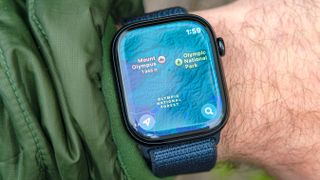 Apple Watch Series 10 on a user's wrist showing the Map app; a topographic map of Olympic National Park is shown