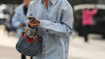 A fashion week guest wearing denim dress, gold earrings and a LV pattern denim handbag 