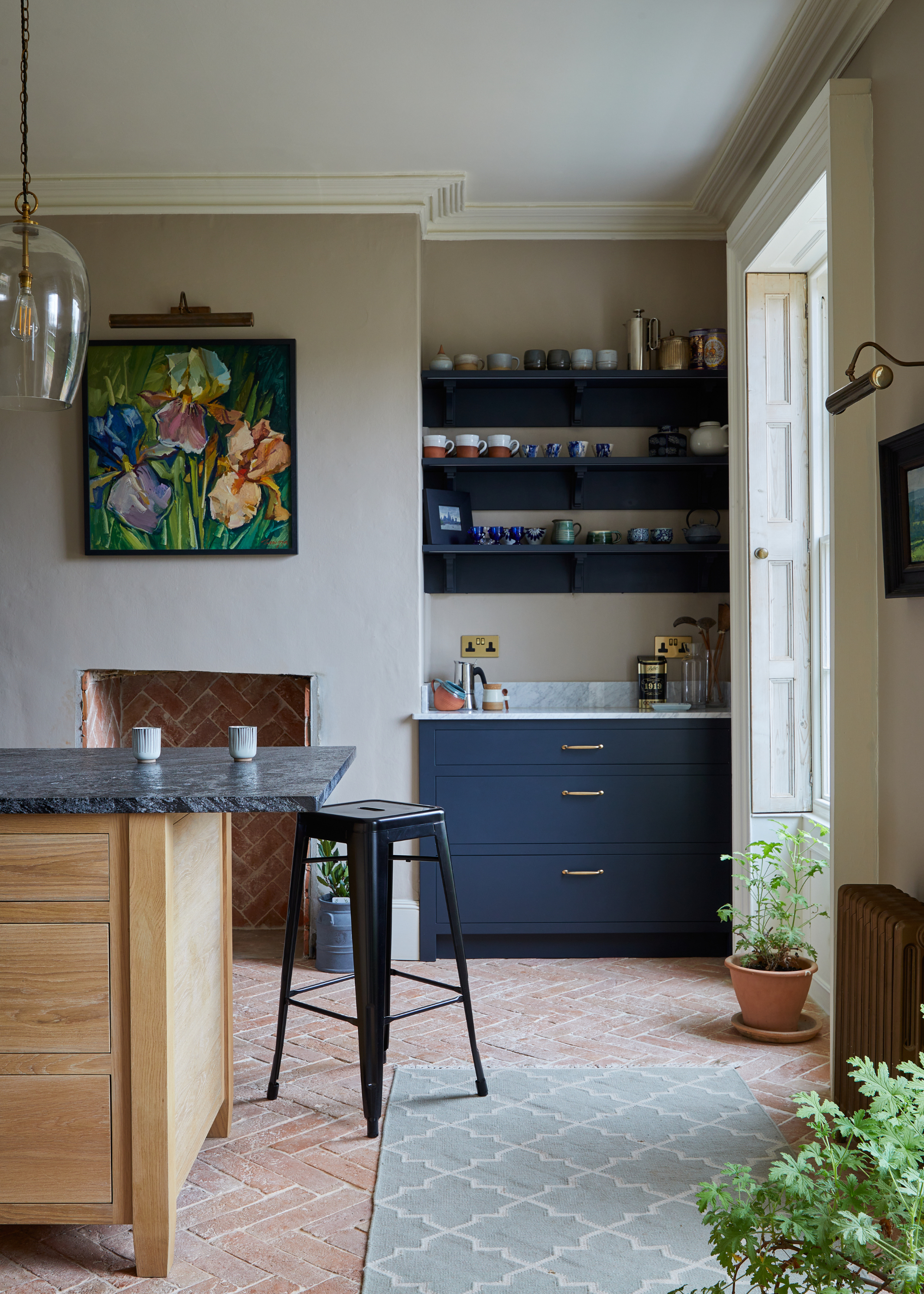 A traditional kitchen with high ceilings, a non-funxtional fireplace , dark blue and marble open shelving in the alcove and a wooden kitchen island