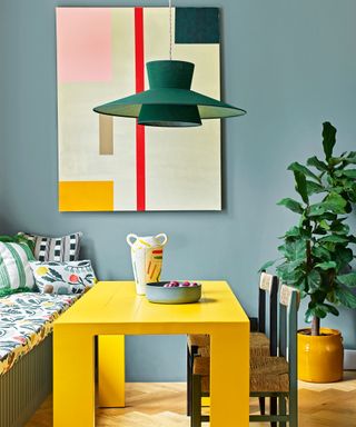 blue dining area with abstract art, yellow table and houseplant