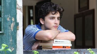 Timothee Chalamet sits on top of books staring out of a window in Call Me By Your Name