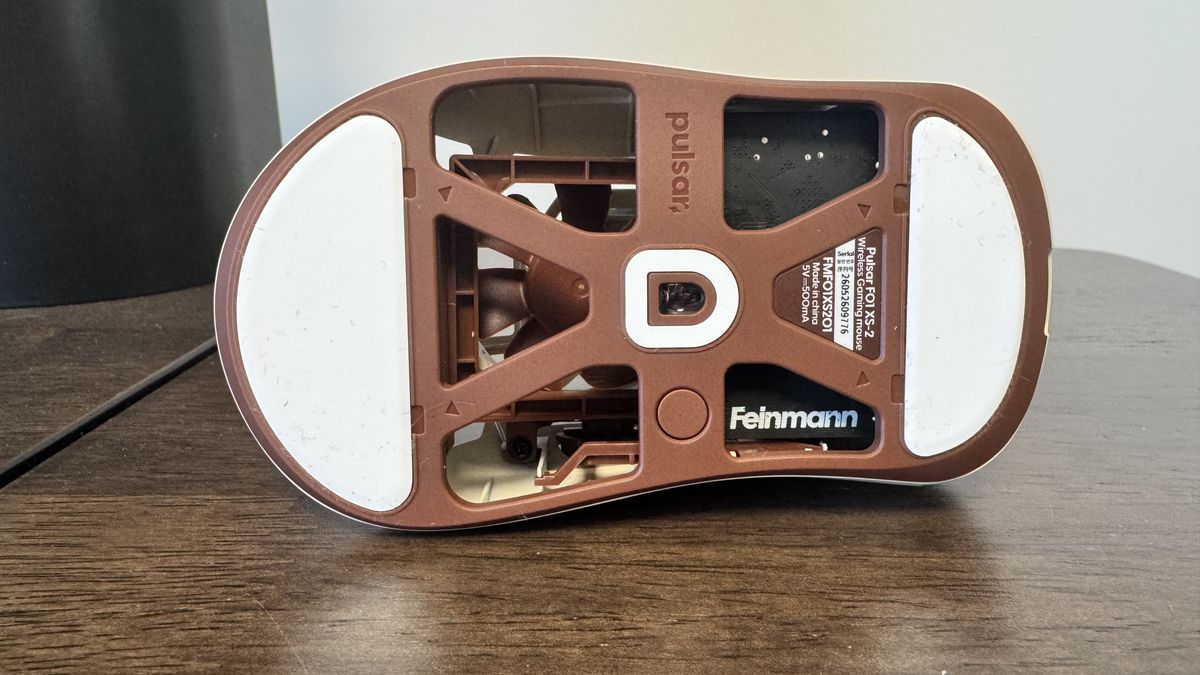 The Pulsar Feinmann F01 Noctua Edition gaming mouse on a wooden desk, from the bottom, showing the Feinmann logo
