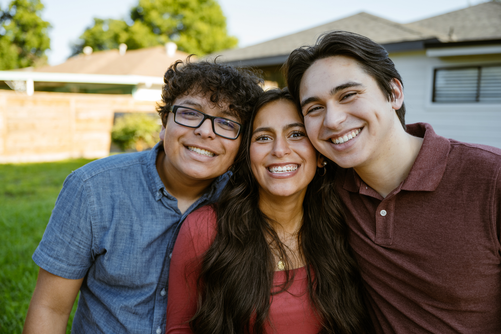 Gen Z siblings are looking at the camera in the front yard of their house and smiling.