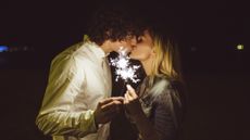 A man and woman holding a sparkler and kissing