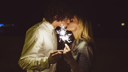 A man and woman holding a sparkler and kissing