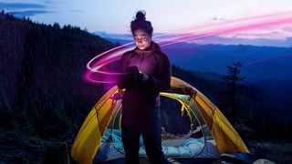 A woman standing in front of a tent using T-Mobile's satellite internet service