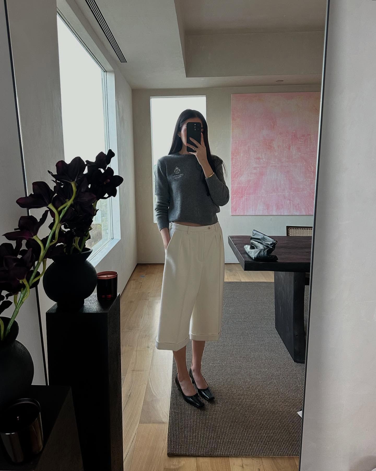 Georgina Downe wearing a gray sweater, cream tailored culotte shorts, and black shoes.