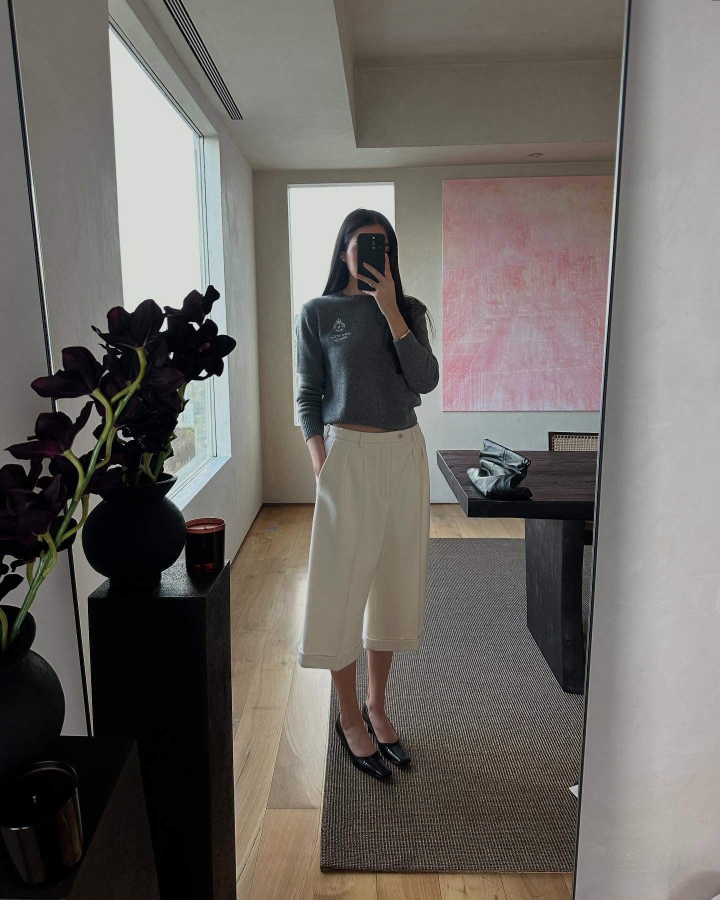 Georgina Downe wearing a gray sweater, cream tailored culotte shorts, and black shoes.