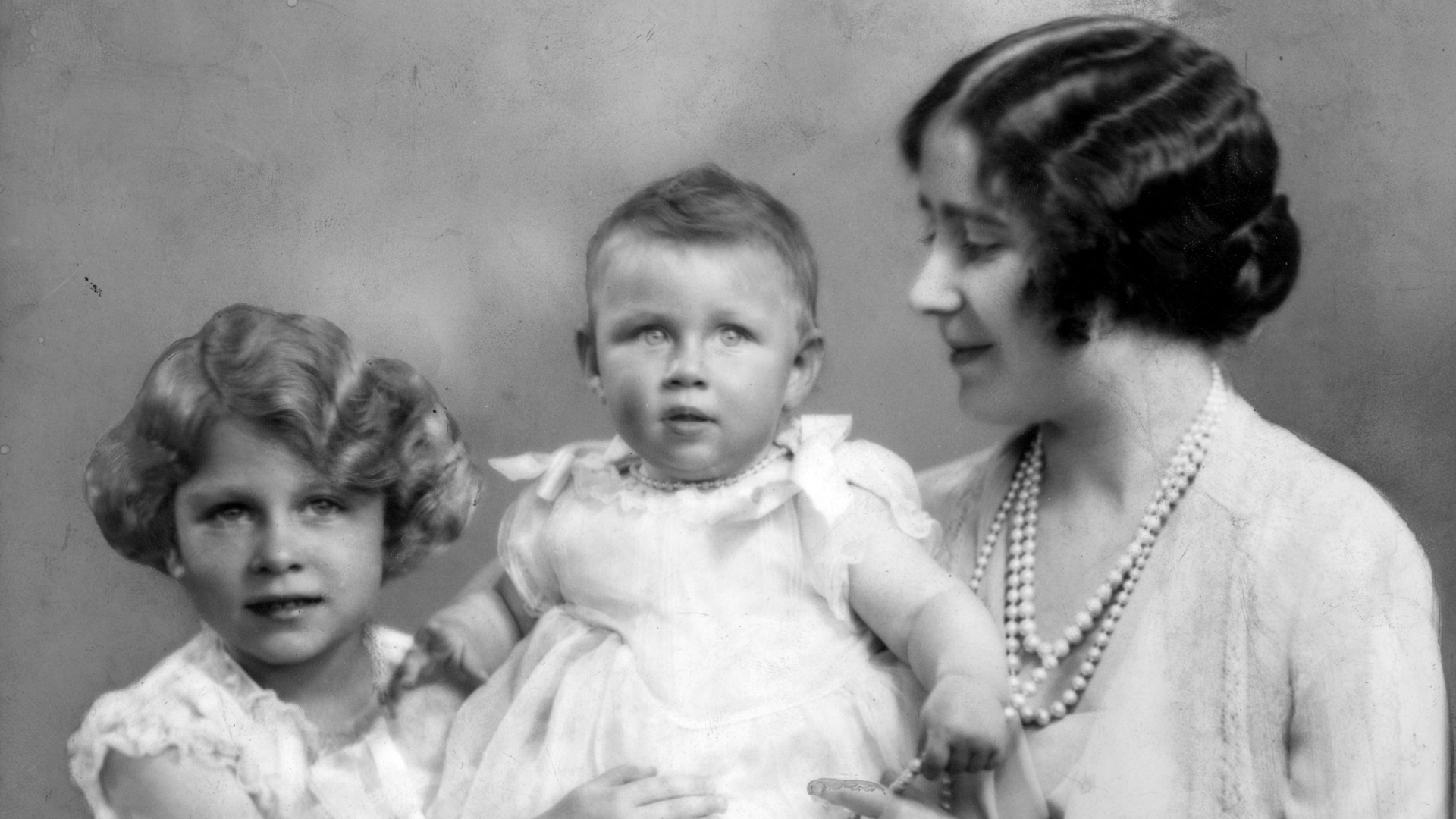 Princess Elizabeth holding Princess Margaret as a baby, watched on by the Queen Mother