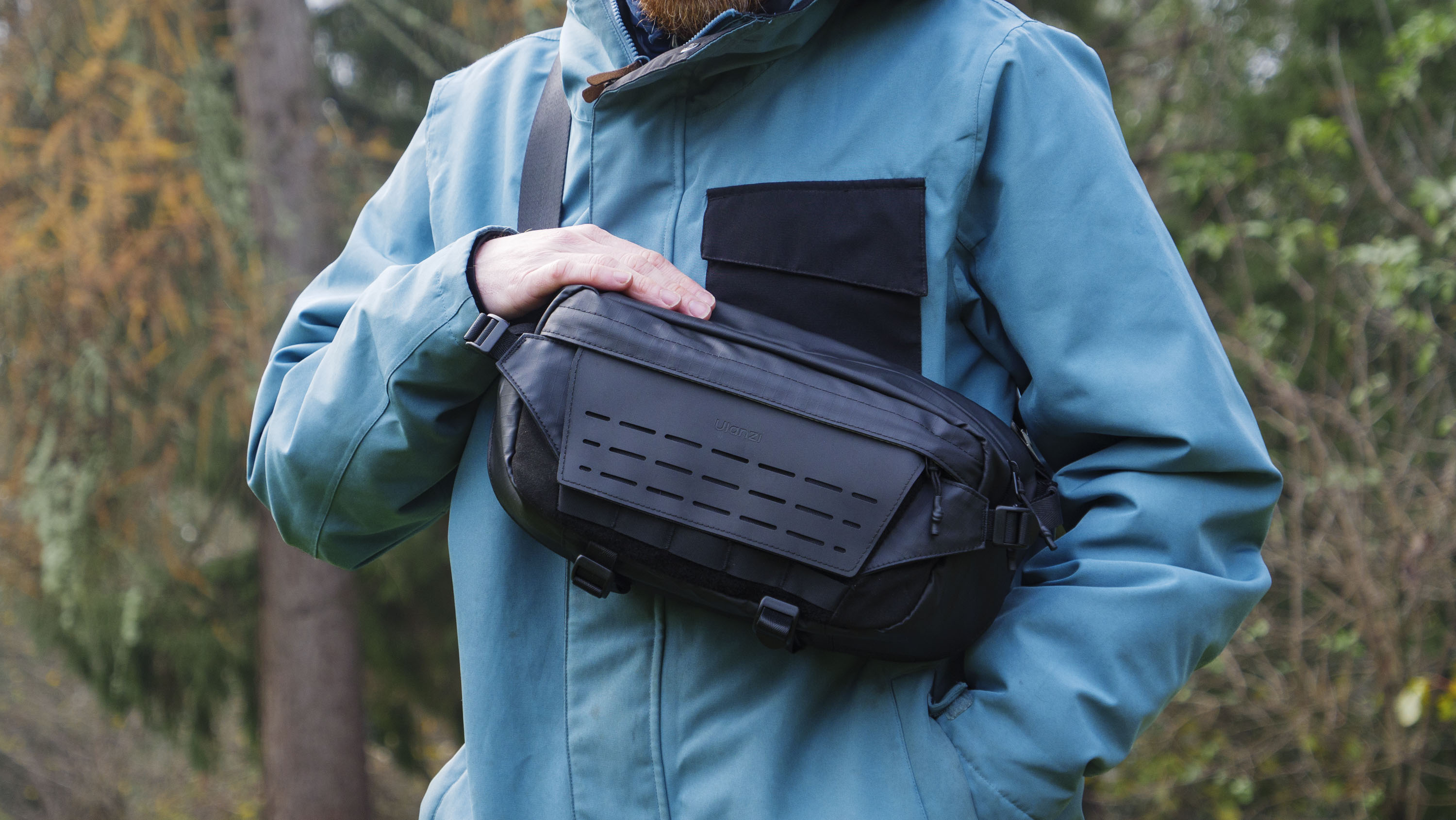 Man wearing a blue jacket outside with a Ulanzi Camera Sling Bag over his shoulder and resting on his midriff