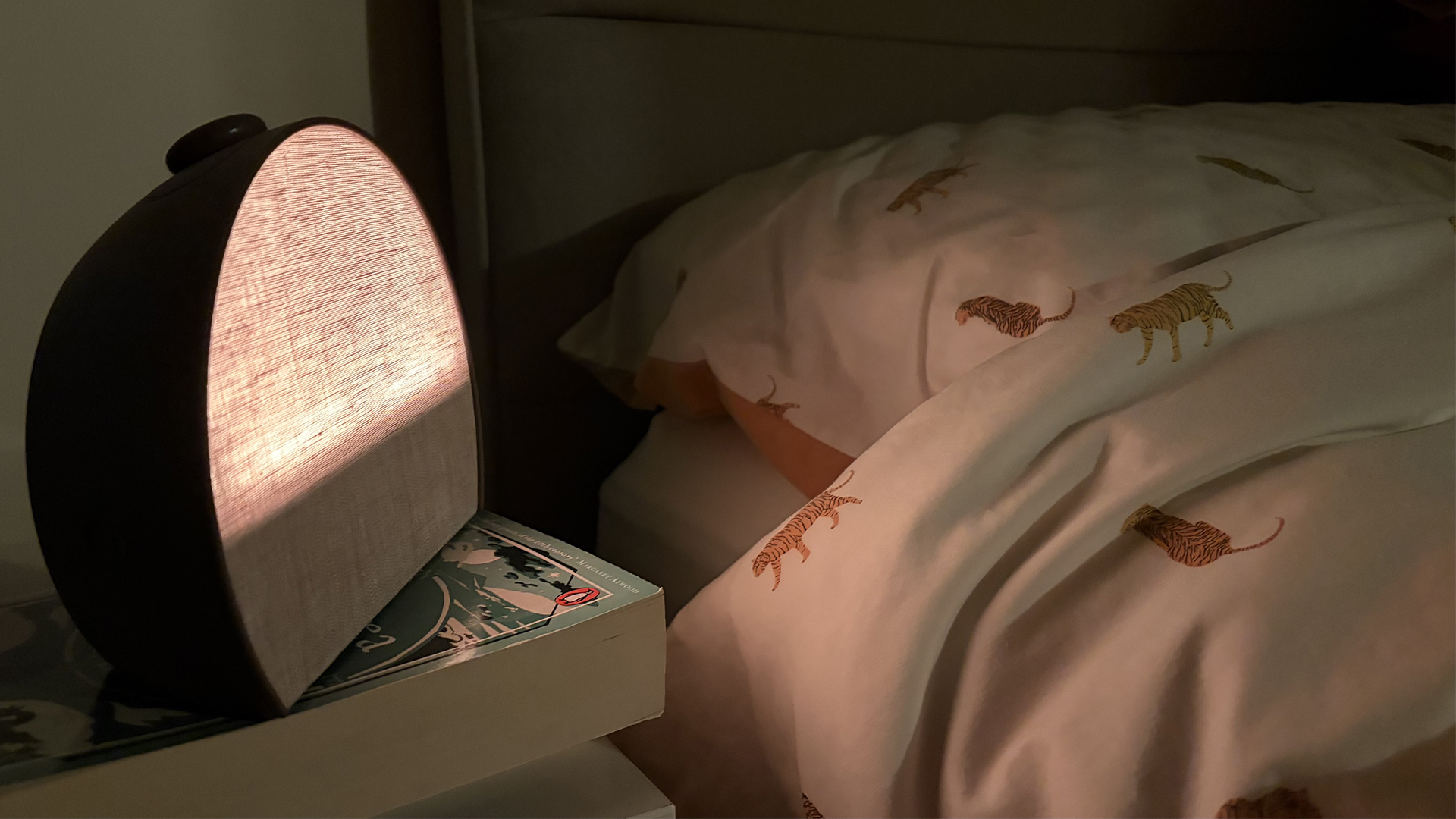 The Hatch Sleep Clock glowing gently yellow next to a bed in a dark room