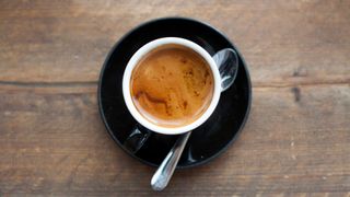 Freshly brewed espresso in black coffee mug sitting on wooden table