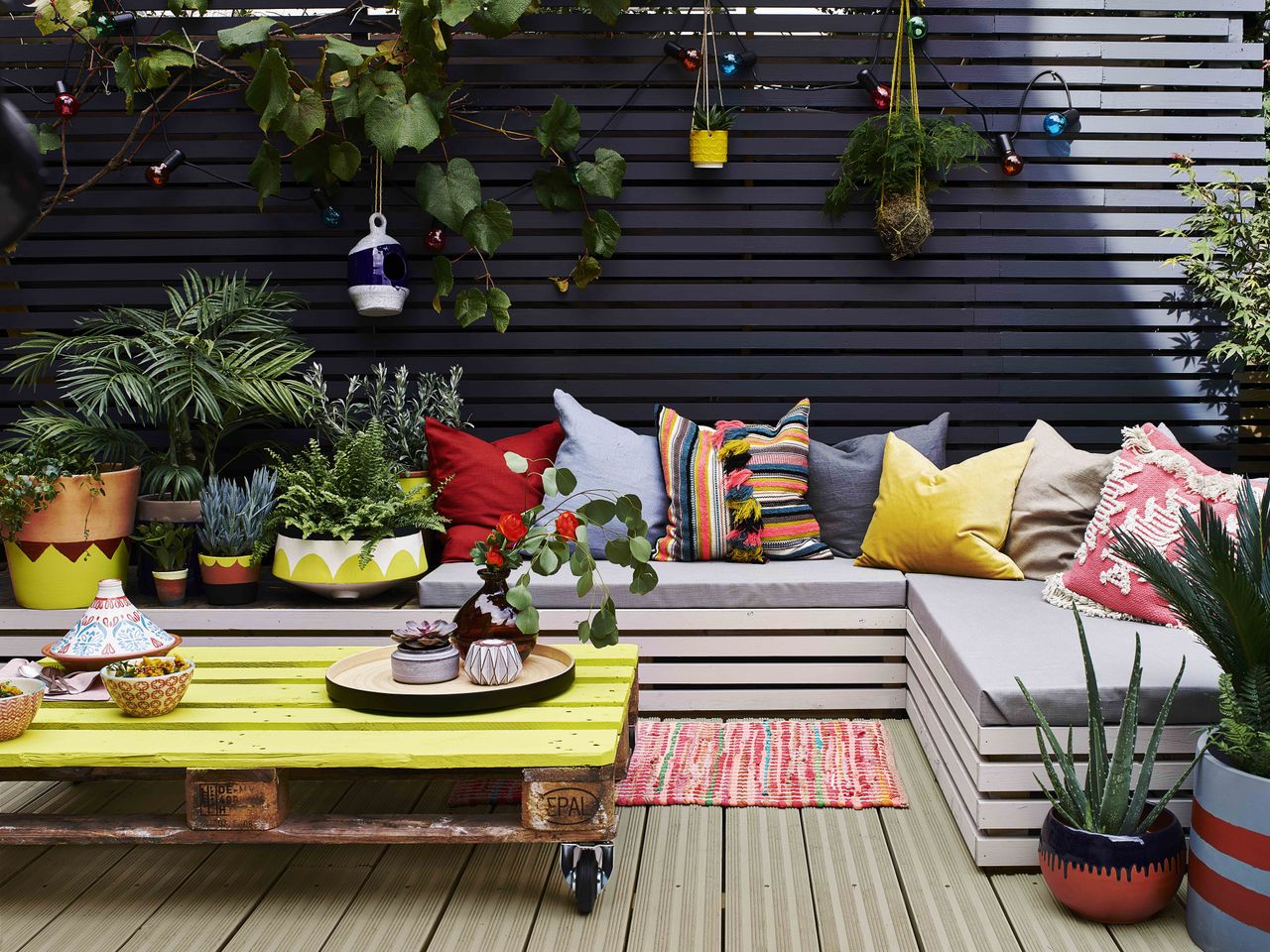 a summery garden decking area with a sofa and cushions, painted in one of the best decking paints: Cuprinol UK