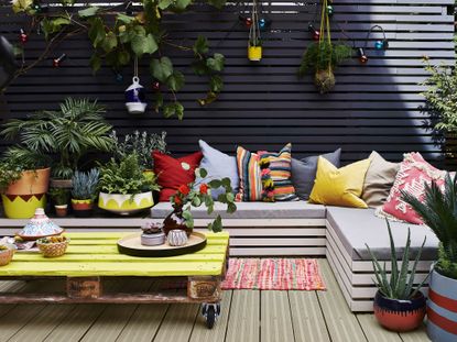 a summery garden decking area with a sofa and cushions, painted in one of the best decking paints: Cuprinol UK