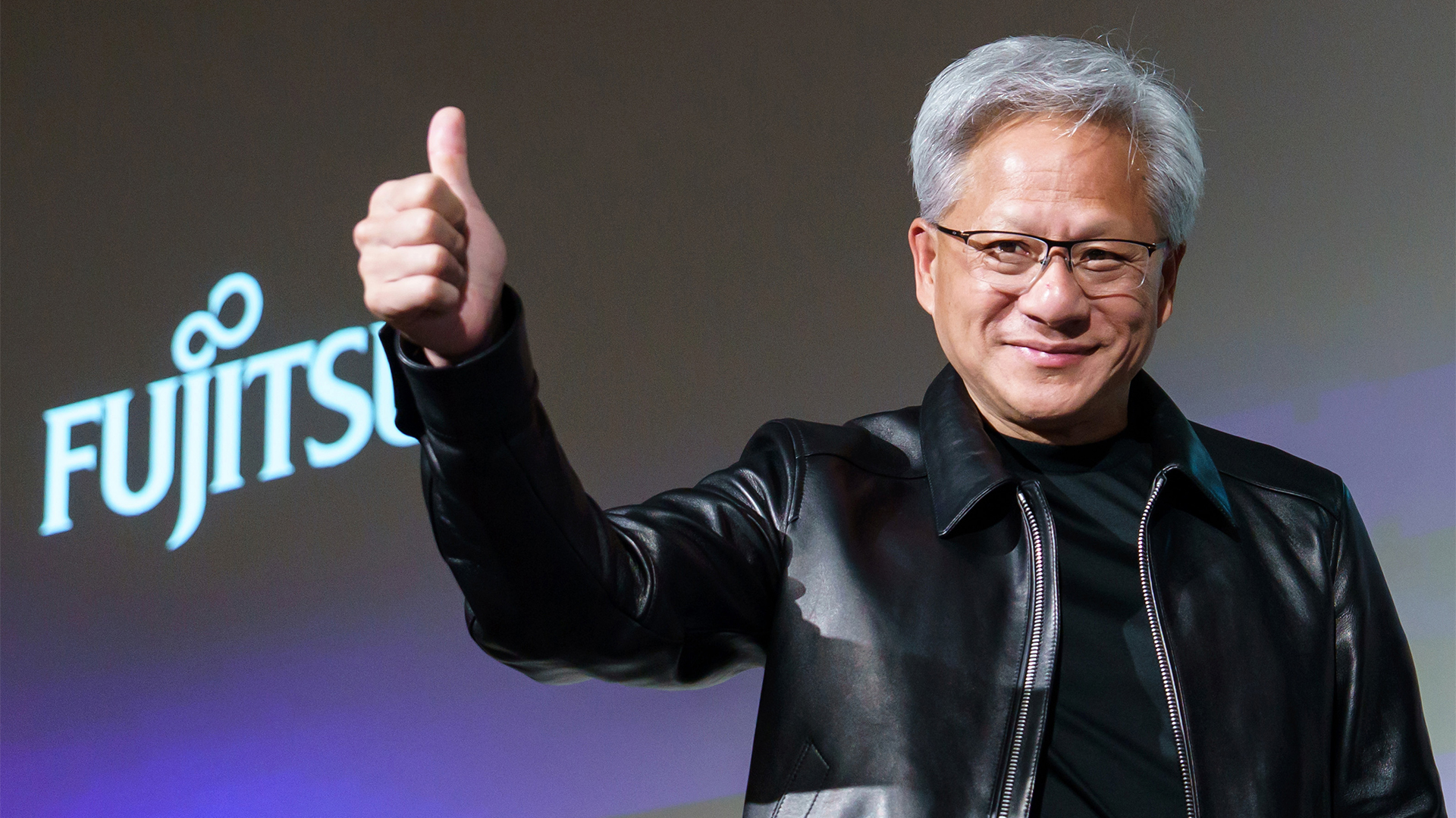 Nvidia CEO Jensen Huang pictured in his signature leather jacket giving a thumbs up during a photo session following a joint press conference with representatives of Fujitsu.