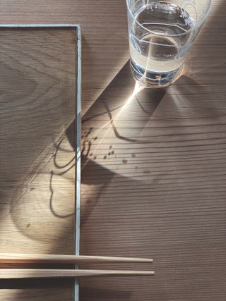 A glass of water on a wooden table next to chop sticks