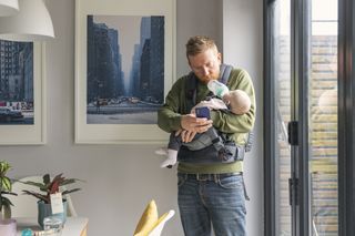 dad feeding baby at home with phone in his hand