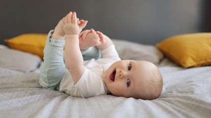 A six-month-old baby grabs his toes while lying on his back.