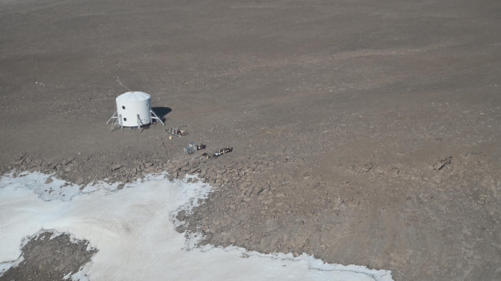 a white tent-like structure sits a rocky barren landscape as seen from the air